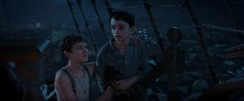Movie still from “Pan” (2015), directed by Joe Wright – Two young men standing next to each other in front of a fence; Medium shot, High angle