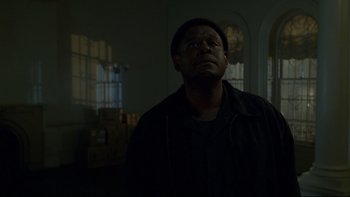 Movie still from “Panic Room” (2002), directed by David Fincher – A man standing in a dark room looking up; Close Up shot, Low angle