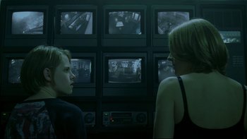 Movie still from “Panic Room” (2002), directed by David Fincher – Two women are looking at a wall of television monitors; Medium shot, Over the shoulder angle