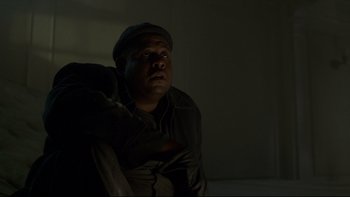 Movie still from “Panic Room” (2002), directed by David Fincher – A man sitting on a couch in a dark room; Medium shot, Low angle