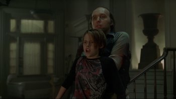 Movie still from “Panic Room” (2002), directed by David Fincher – A man and a boy are standing in a dark room; Medium shot, Low angle