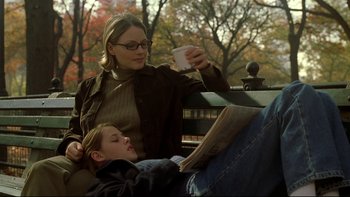 Movie still from “Panic Room” (2002), directed by David Fincher – A woman sitting next to a child reading a newspaper; Medium shot, High angle