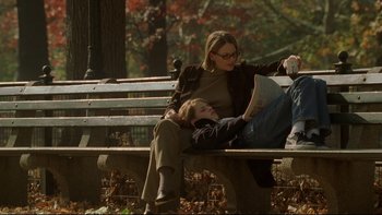 Movie still from “Panic Room” (2002), directed by David Fincher – A woman sitting on top of a wooden bench next to a man; Wide shot, Low angle
