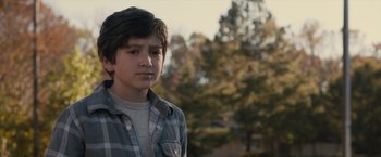 Movie still from “Paper Towns” (2015), directed by Jake Schreier – A young boy in a plaid shirt is standing in front of trees; Close Up shot, Over the shoulder angle