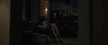 Movie still from “Paper Towns” (2015), directed by Jake Schreier – A young man sitting on the floor playing a video game; Wide shot, High angle