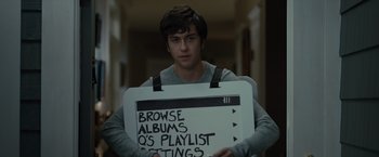 Movie still from “Paper Towns” (2015), directed by Jake Schreier – A young man holding up a sign that says " browse albums q's playlist ratings "; Medium shot, Over the shoulder angle