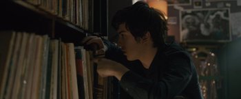 Movie still from “Paper Towns” (2015), directed by Jake Schreier – A young man looking at a book on a shelf; Close Up shot, Over the shoulder angle