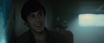 Movie still from “Paper Towns” (2015), directed by Jake Schreier – A young man smiling for the camera in a dark room; Close Up shot, Over the shoulder angle