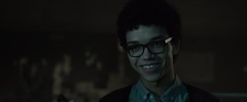 Movie still from “Paper Towns” (2015), directed by Jake Schreier – A young man wearing glasses smiling for the camera; Close Up shot, Over the shoulder angle