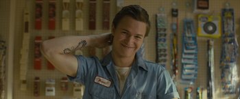 Movie still from “Paper Towns” (2015), directed by Jake Schreier – A man with a tattoo on his arm is smiling for the camera; Close Up shot, Low angle