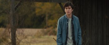 Movie still from “Paper Towns” (2015), directed by Jake Schreier – A young man standing in a field with trees in the background; Medium shot, Over the shoulder angle