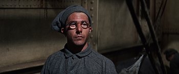 Movie still from “Papillon” (1973), directed by Franklin J. Schaffner – A man wearing glasses and wearing a hat; Close Up shot, Low angle