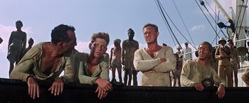 Movie still from “Papillon” (1973), directed by Franklin J. Schaffner – A group of men standing next to each other on top of a boat; Medium shot, Low angle