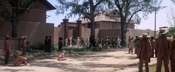 Movie still from “Papillon” (1973), directed by Franklin J. Schaffner – A group of people standing in front of a building; Extreme Wide shot, High angle