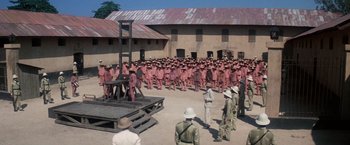 Movie still from “Papillon” (1973), directed by Franklin J. Schaffner – A group of men in red uniforms standing around a prison; Extreme Wide shot, High angle