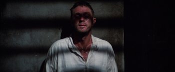 Movie still from “Papillon” (1973), directed by Franklin J. Schaffner – A man in a white shirt is standing in front of a brick wall; Close Up shot, Low angle