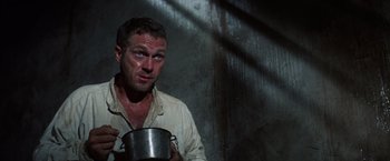 Movie still from “Papillon” (1973), directed by Franklin J. Schaffner – A man holding a metal pot in a dark room; Medium shot, Low angle