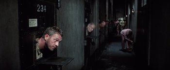Movie still from “Papillon” (1973), directed by Franklin J. Schaffner – A group of men standing next to each other in a room; Wide shot, High angle