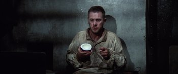 Movie still from “Papillon” (1973), directed by Franklin J. Schaffner – A man sitting down holding a cup in his hands; Medium shot, High angle
