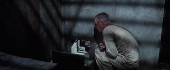 Movie still from “Papillon” (1973), directed by Franklin J. Schaffner – An older man sitting in a dark room next to a laptop computer; Medium shot, High angle