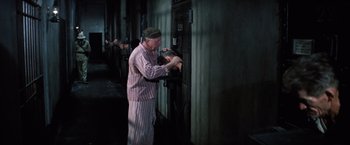 Movie still from “Papillon” (1973), directed by Franklin J. Schaffner – An old man in a striped pajamas is fixing a light switch; Medium shot, High angle