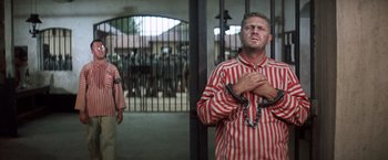 Movie still from “Papillon” (1973), directed by Franklin J. Schaffner – A man in a striped shirt with chains around his neck; Medium shot, Low angle