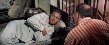 Movie still from “Papillon” (1973), directed by Franklin J. Schaffner – A man sitting on the ground in a jail cell; Medium shot, High angle