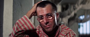 Movie still from “Papillon” (1973), directed by Franklin J. Schaffner – A person wearing glasses and a striped shirt; Close Up shot, Low angle