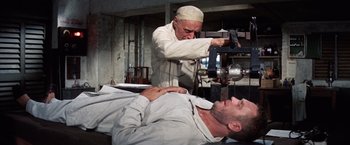 Movie still from “Papillon” (1973), directed by Franklin J. Schaffner – A man is getting his head shaved by an old man; Medium shot, Low angle