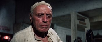 Movie still from “Papillon” (1973), directed by Franklin J. Schaffner – An old man wearing a head covering looking sad; Close Up shot, Low angle