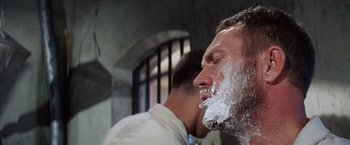 Movie still from “Papillon” (1973), directed by Franklin J. Schaffner – A man shaving his face while another man looks on; Close Up shot, Low angle