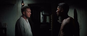 Movie still from “Papillon” (1973), directed by Franklin J. Schaffner – Two men are facing each other in a dark room; Medium shot, Over the shoulder angle