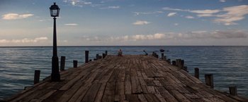 Movie still from “Papillon” (1973), directed by Franklin J. Schaffner – A person sitting on a dock looking out at the ocean; Extreme Wide shot, High angle