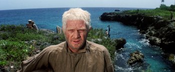 Movie still from “Papillon” (1973), directed by Franklin J. Schaffner – An older man with white hair standing in front of a body of water; Close Up shot, Low angle