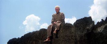 Movie still from “Papillon” (1973), directed by Franklin J. Schaffner – An older man sitting on top of a rock; Wide shot, Low angle