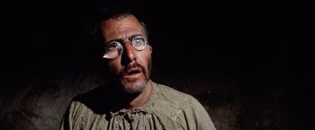 Movie still from “Papillon” (1973), directed by Franklin J. Schaffner – A man with glasses and a beard wearing glasses; Close Up shot, Low angle