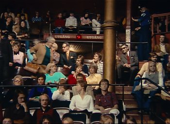 Movie still from “Parade” (1974), directed by Jacques Tati – A group of people sitting in a room; Extreme Wide shot, High angle