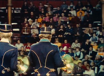Movie still from “Parade” (1974), directed by Jacques Tati – A man in a blue uniform is playing a musical instrument in front of an audience; Medium shot, High angle