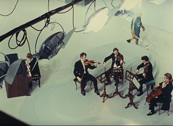 Movie still from “Parade” (1974), directed by Jacques Tati – A group of people sitting around playing musical instruments; Extreme Wide shot, High angle