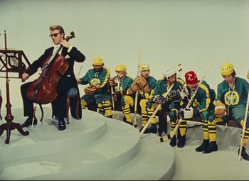 Movie still from “Parade” (1974), directed by Jacques Tati – A group of hockey players and a man with a cello; Wide shot, High angle