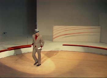 Movie still from “Parade” (1974), directed by Jacques Tati – A man in a suit and hat on a stage; Extreme Wide shot, High angle
