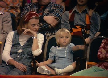 Movie still from “Parade” (1974), directed by Jacques Tati – A woman sitting next to a little girl in a crowd; Medium shot, High angle