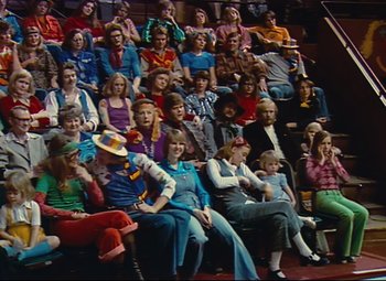 Movie still from “Parade” (1974), directed by Jacques Tati – A group of people sitting in a row on a stage; Wide shot, High angle