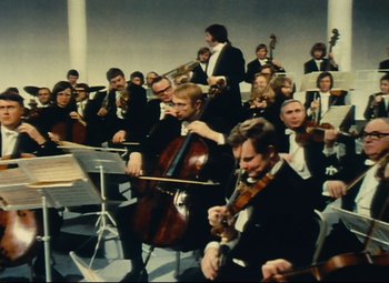 Movie still from “Parade” (1974), directed by Jacques Tati – A group of people that are sitting in a room with instruments; Wide shot, Low angle