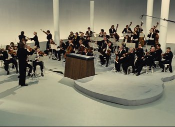 Movie still from “Parade” (1974), directed by Jacques Tati – A group of people sitting around a stage with instruments; Extreme Wide shot, High angle
