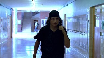 Movie still from “Paranoid Park” (2007), directed by Gus Van Sant – A woman in a black shirt and a black hat is walking down a hall way; Medium shot, Low angle