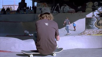 Movie still from “Paranoid Park” (2007), directed by Gus Van Sant – A man sitting on a skateboard in a skate park; Wide shot, High angle