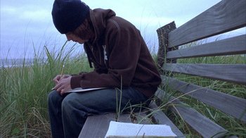 Movie still from “Paranoid Park” (2007), directed by Gus Van Sant – A man sitting on top of a wooden bench writing; Medium shot, High angle