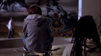Movie still from “Paranoid Park” (2007), directed by Gus Van Sant – A person sitting on top of a skate board; Medium shot, Over the shoulder angle