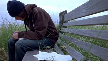 Movie still from “Paranoid Park” (2007), directed by Gus Van Sant – A person sitting on a bench in a grassy field; Medium shot, Low angle